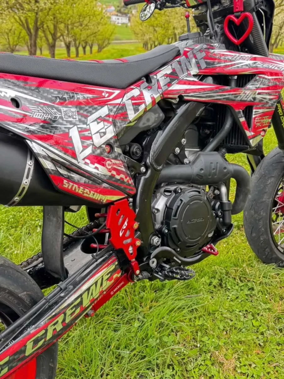 Supermotard avec kit déco HRL rouge, argent et carbone, vu de côté dans un verger